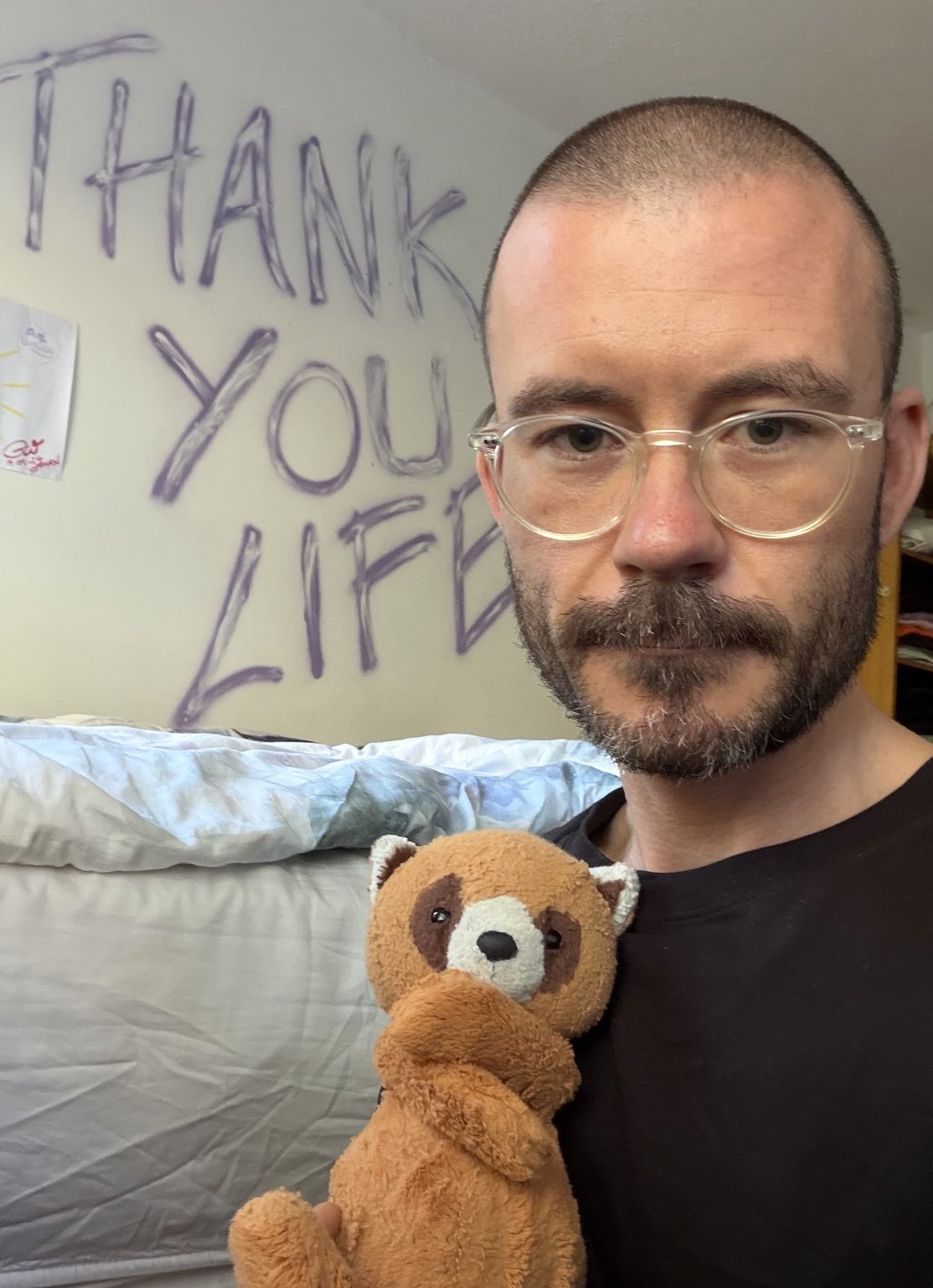 Paul Walsh holding his teddy, with Thank You Life written on the wall behind him